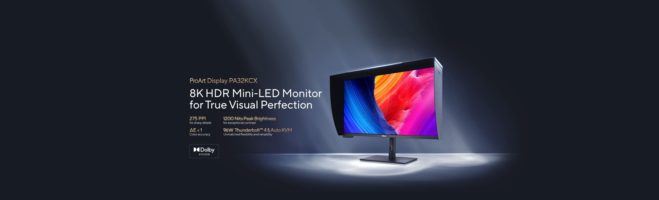 A professional ASUS ProArt monitor featuring a built-in motorized colorimeter and a protective shading hood. The display shows a vibrant, high-contrast image of colorful rock formations in blue, orange, and magenta, standing on a dark surface illuminated by dramatic spotlights.